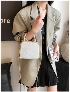 Detail of silver crossbody bag with gold frame and chain strap worn on stylish outfit
