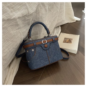 Detail of vintage denim handbag featuring brown leather trim and metal rivet accents