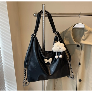 Close-up of black leather bag with white bow, woven chain, and plush cloud charm