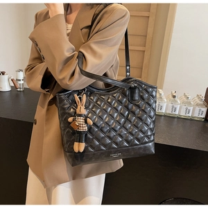 Details einer schwarzen Stepp-Eimertasche mit Plüschhasen-Anhänger und Aufschrift