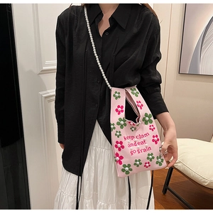 Detail of pink knitted bucket bag with floral accents and white pearl chain strap