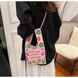 Detail of pink knitted bucket bag with floral patterns and pearl chain strap on model