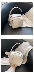 Nahaufnahme der weißen geflochtenen Eimer-Tasche mit geometrischen Würfeln und Silberkette