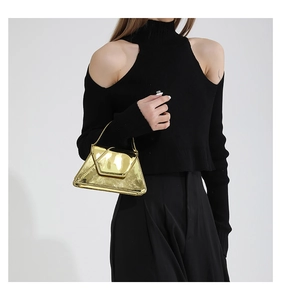 Detail of a metallic gold trapezoid handbag paired with a black off-shoulder knit top