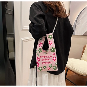 Detail of pink knitted tote bag featuring floral patterns and a pearl bead shoulder strap