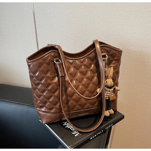 Brown quilted tote bag with rabbit charm detail and white text on a black magazine