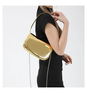 Close-up of golden patent leather handbag featuring mirror finish and silver bead chain