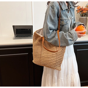 Detail view of woven straw tote bag with brown leather straps shown on a shoulder