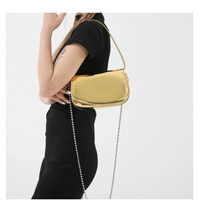 Close-up of golden metallic patent leather bag with slim ball chain on black dress