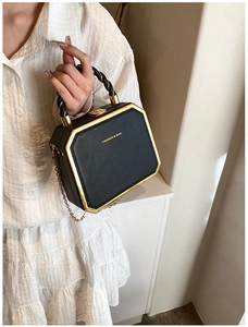 Detail of a black hexagonal hardshell bag with gold metal frame and rope handle