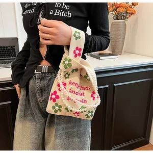 Close-up of beige knit bucket bag with floral patterns and elegant pearl handle detail