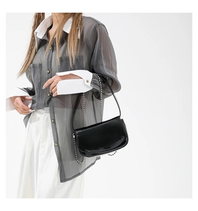 Detail of minimalist black patent leather shoulder bag with silver bead chain strap