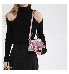Close-up of pink patent leather handbag with metallic finish and geometric shape on model