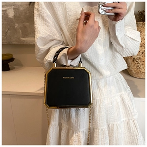 Detail of elegant black box bag with gold metal frame and woven handle on white dress