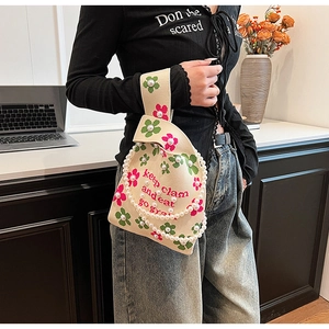 Detailed view of knitted bucket bag with clover print and pearl chain handle decoration