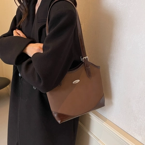 Brown leather underarm shoulder bag with metal detail shown on a model in a black coat