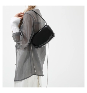 Detail of black patent leather handbag with silver metallic bead chain and glossy finish