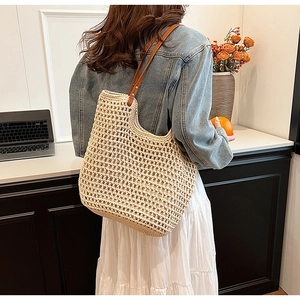 Detail of hollow-out beige straw tote bag featuring brown leather handles and metal rivets
