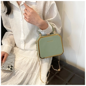 Detail of light green hexagonal box bag with gold metal trim and elegant chain strap