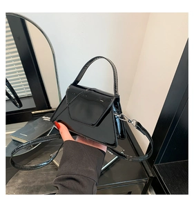 Close-up of a trapezoid black patent leather bag with a glossy finish and metal clasps