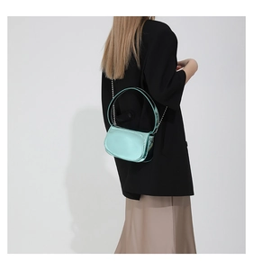 Mint green patent leather handbag with chain strap shown on a model in a studio setting