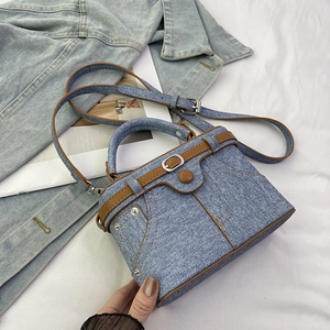 Detail of denim box bag featuring contrast stitching, metal rivets and brown leather strap