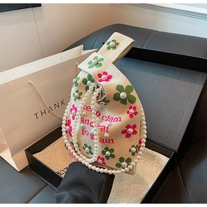Detail of beige knit bucket bag with floral pearls and a decorative pearl chain handle