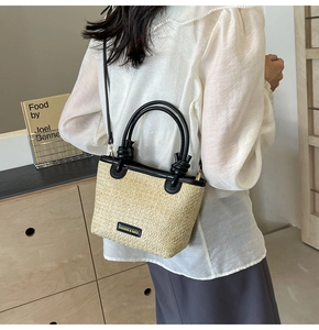 Detail of a beige woven straw bucket bag with black leather handles and knot accents