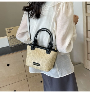 Close-up of woven straw handbag featuring black knotted leather handle and brand tag detail