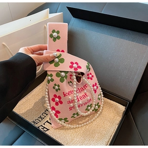 Close-up of pink knit bucket bag with floral patterns, pearls, and luxury gold chain