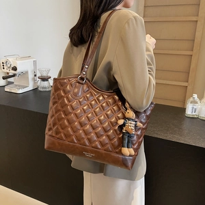 Braune gesteppte Tragetasche mit Bärenanhänger am Model in einem minimalistischen Café