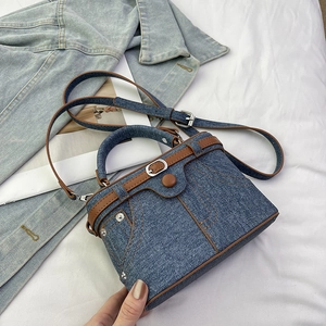 Close-up of blue denim and brown leather patchwork bag with metal studs and buckle