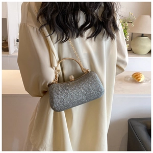 Silver glitter evening clutch bag with gold handle held by a model in elegant interior