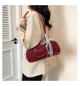 Detail of dark red crescent bag with ripple texture and lace bow on a shoulder