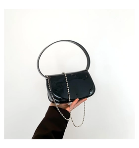 Close-up of black patent leather handbag with silver bead chain and rigid handle