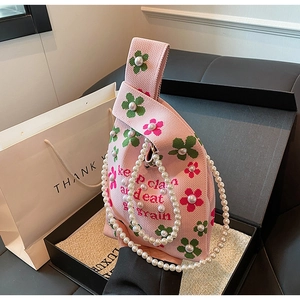 Detail of pink knitted bucket bag featuring floral patterns and elegant pearl chain strap