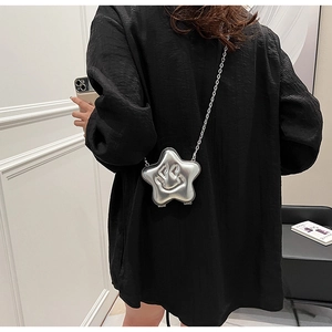 Detail view of a silver star-shaped crossbody bag with embossed smiley on a black outfit