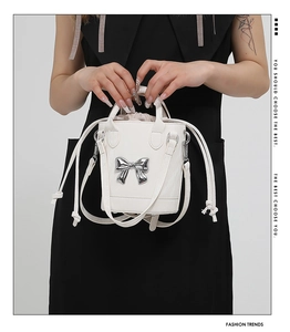 Detail of white mini bucket bag featuring a silver bow and stylish drawstring inner pouch