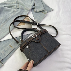 Close-up of denim handbag featuring brown leather piping and vintage stitching details