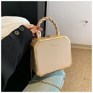 Detail of elegant beige octagonal hard shell bag with golden metal trim and chain strap