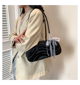 Detail of black PU leather shoulder bag with decorative lace bow and wavy texture pattern