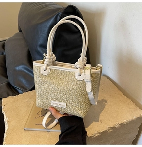 Detailed macro view of woven straw bucket bag with white faux leather handles and metal hardware