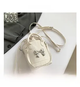 Detail view of cream bucket bag showing silver bow ornament and drawstring closure
