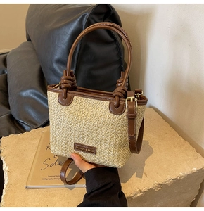 Close-up of beige straw weave bag with brown leather handles and brand metal plaque