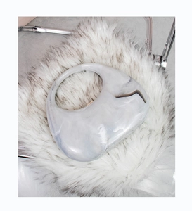 Detail of marble pattern acrylic handbag with circular handle on white faux fur