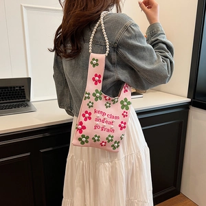 Pink knitted bucket bag with floral patterns and pearl strap on model's shoulder