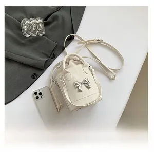 Close-up of cream mini bucket bag with silver bow hardware and drawstring closure