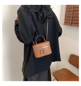 Dettaglio borsa vanity marrone a trama intrecciata con tracolla a catena dorata su blazer nero