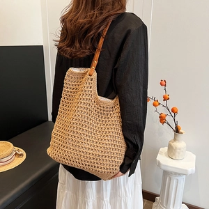 Handwoven straw tote bag with brown leather shoulder strap in a minimalist style
