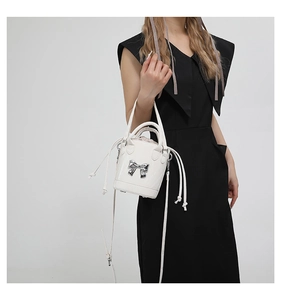Detail of white glossy bucket bag with silver bow ornament and drawstring inner bag